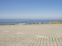 view of ocean and a beach from a bench at a park with sand and brick walkways