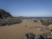 a sandy beach with boulders on a clear day in the sun with blue sky in back