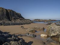 a sandy beach with boulders on a clear day in the sun with blue sky in back