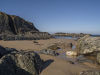 a sandy beach with boulders on a clear day in the sun with blue sky in back