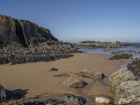 a sandy beach with boulders on a clear day in the sun with blue sky in back