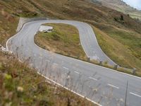 the truck is going around the bend of the hill road between hills and grass and the road is winding through the hills