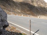 there is a man riding a motorcycle on the street near a cliff wall with a hill behind him