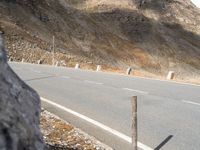 there is a man riding a motorcycle on the street near a cliff wall with a hill behind him
