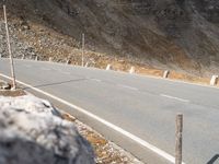 there is a man riding a motorcycle on the street near a cliff wall with a hill behind him