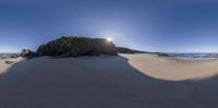 a very large rock at the ocean beach with sun light shining on the side of it