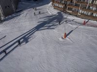 a skier jumps a hill next to a building in ski resort snow covered slopes with skiiers