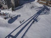 a skier jumps a hill next to a building in ski resort snow covered slopes with skiiers