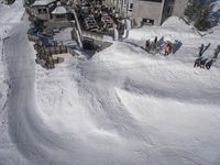 a skier jumps a hill next to a building in ski resort snow covered slopes with skiiers