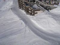 a skier jumps a hill next to a building in ski resort snow covered slopes with skiiers