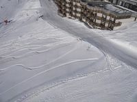 a skier jumps a hill next to a building in ski resort snow covered slopes with skiiers