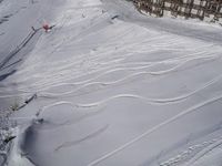 a skier jumps a hill next to a building in ski resort snow covered slopes with skiiers