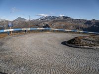 a gravel road in front of mountains and buildings with the sky over them, and two people standing on it