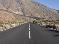 a road in front of the mountains with no traffic signs on it and grass growing along the side