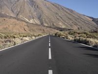 a road in front of the mountains with no traffic signs on it and grass growing along the side