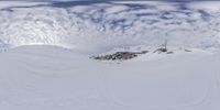 the view from below of a snow boarder and ski in the distance with some snow capped mountains behind