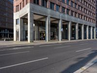 the long building is built with cement and glass windows on it's sides and two people riding bikes on either side