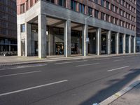 the long building is built with cement and glass windows on it's sides and two people riding bikes on either side