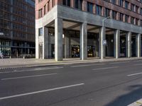 the long building is built with cement and glass windows on it's sides and two people riding bikes on either side