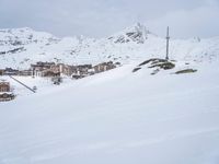 a snow covered slope has skiers and buildings in the background on a mountaintop