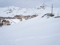 a snow covered slope has skiers and buildings in the background on a mountaintop