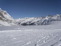 person on skis on slope with snow mountains in background / snowy slopes and ski tracks in foreground