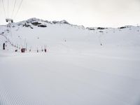 a man on skis going down the side of a snowy hill near some ski lift poles