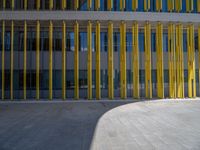 a concrete structure made into rows of orange and yellow poles are on a cement sidewalk