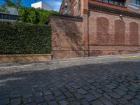 a long empty brick street with tall buildings in the background on a sunny day with some people walking around