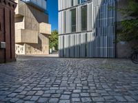 cobblestone driveway surrounded by modern buildings on sunny day with sun reflecting onto the windows