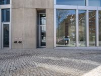 a building with two double doors and windows on a brick floor outside it and there are windows with some reflection in the glass