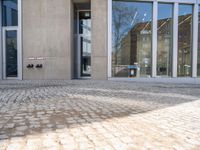 a building with two double doors and windows on a brick floor outside it and there are windows with some reflection in the glass