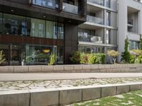 a bench on the side of a concrete building and grass next to the sidewalk area