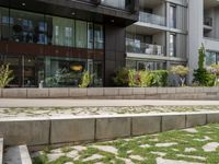 a bench on the side of a concrete building and grass next to the sidewalk area