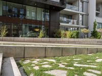 a bench on the side of a concrete building and grass next to the sidewalk area