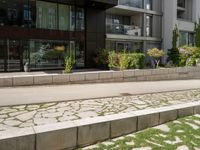 a bench on the side of a concrete building and grass next to the sidewalk area