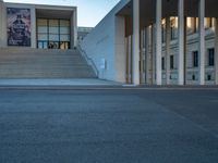 empty street lined with cement buildings next to a tall building with a staircase up to it