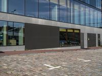 a gray building with windows and a small door on the sidewalk with a bench outside