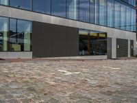 a gray building with windows and a small door on the sidewalk with a bench outside