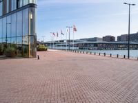 a red brick sidewalk next to water and a walkway leading up to a glass building