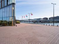 a red brick sidewalk next to water and a walkway leading up to a glass building