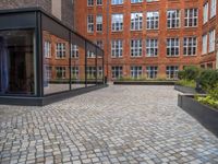 an empty parking lot with plants in the ground and on the side of the building, there is an enclosed area and windows