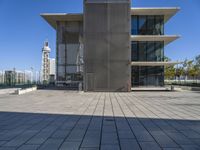 a long concrete building on top of a sidewalk next to a big metal tower that has a bench underneath it