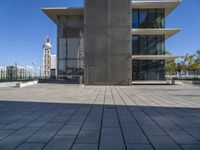 a long concrete building on top of a sidewalk next to a big metal tower that has a bench underneath it