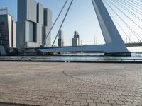 the cyclist is sitting by the side of the river under the bridge, with buildings in the background