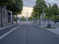 a small empty road in front of some buildings on either side of the road is an alley lined with green trees and trees