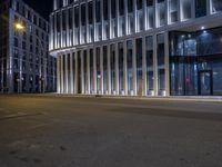 the front view of an office building with illuminated windows and metal columns at night time