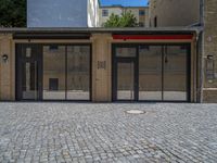 the sidewalk is paved with stones and has a bench in front of it, with no people inside