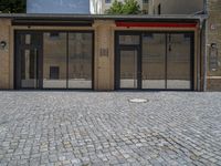 the sidewalk is paved with stones and has a bench in front of it, with no people inside