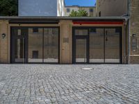 the sidewalk is paved with stones and has a bench in front of it, with no people inside